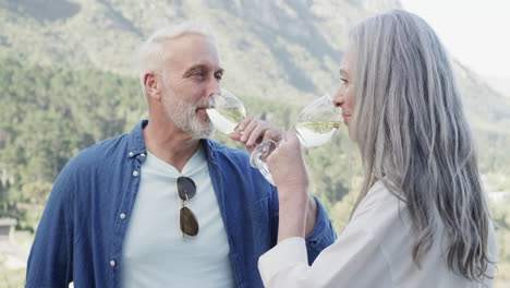 Glückliches-Kaukasisches-Paar-Mittleren-Alters,-Das-Auf-Der-Terrasse-In-Den-Bergen-Wein-Trinkt,-Zeitlupe