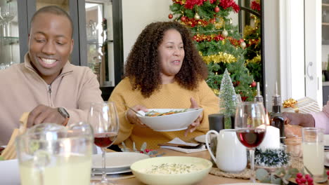 Happy-african-american-mother-serving-food-at-multi-generation-family-christmas-dinner-table