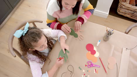 Happy-biracial-mother-and-daughter-cutting-and-sticking-cutouts-in-sunny-living-room
