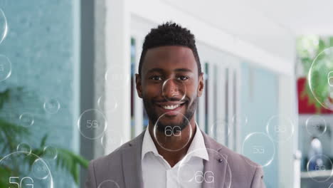 Animation-of-5g-text-in-circles-over-smiling-african-american-businessman-standing-in-office