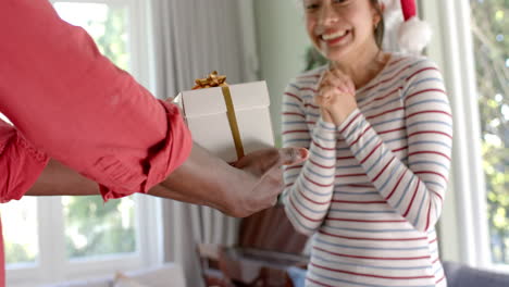 Midsection-of-happy-diverse-couple-exchanging-christmas-gift-at-home,-slow-motion