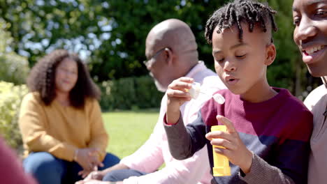 Happy-african-american-parents-with-grandfather-and-son-blowing-bubbles-in-sunny-garden