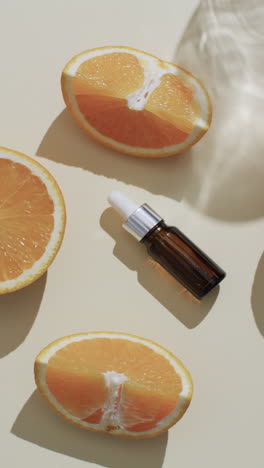 Vertical-video-of-make-up-bottle-with-pipette,-orange-slices-and-copy-space-on-white-background