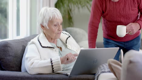 Happy-senior-caucasian-couple-sitting-on-sofa-using-laptop-at-home,-slow-motion