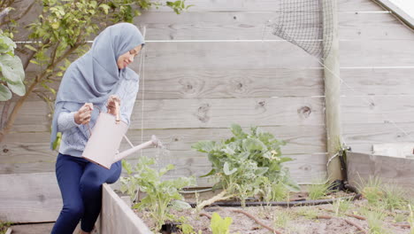 Happy-biracial-woman-in-hijab-watering-plants,-gardening-with-copy-space,-slow-motion