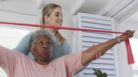 Caucasian-nurse-with-senior-woman-exercising-with-rubber-band,-copy-space,-slow-motion