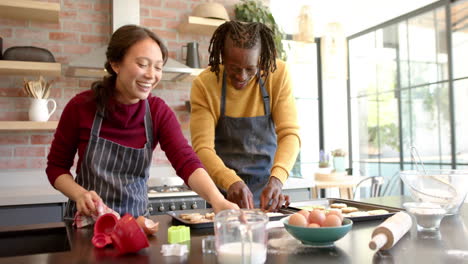 Happy-diverse-couple-in-aprons-baking-christmas-cookies-in-kitchen,-slow-motion