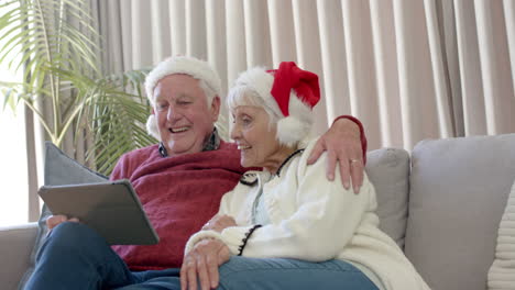 Senior-caucasian-couple-wearing-santa-hats-using-tablet-for-christmas-video-call,-slow-motion