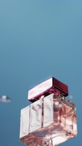 Vertical-video-of-drops-falling-on-beauty-product-bottle-with-copy-space-on-blue-background
