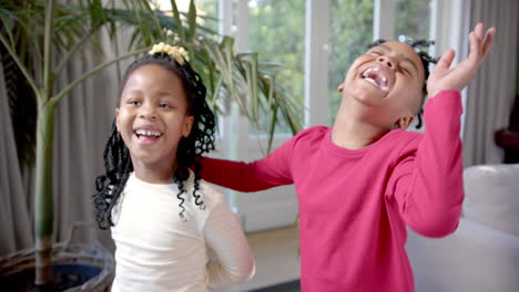 Happy-african-american-brother-and-sister-laughing-and-embracing-in-sunny-living-room,-slow-motion
