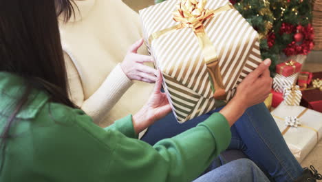 Midsection-of-biracial-mother-and-adult-daughter-exchanging-christmas-gift-at-home,-slow-motion