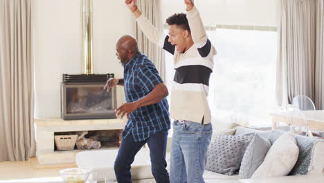 Excited-african-american-father-and-adult-son-watching-sport-on-tv-and-celebrating,-slow-motion