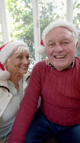 Vertical-video-of-senior-caucasian-couple-wearing-santa-having-christmas-video-call,-slow-motion