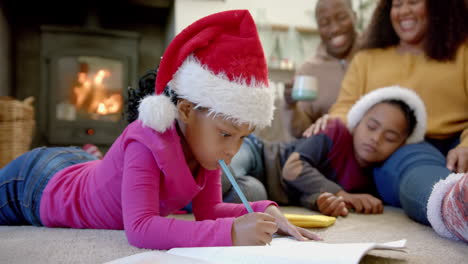 Happy-african-american-daughter-in-christmas-hat-drawing-and-son-asleep-with-parents,-slow-motion