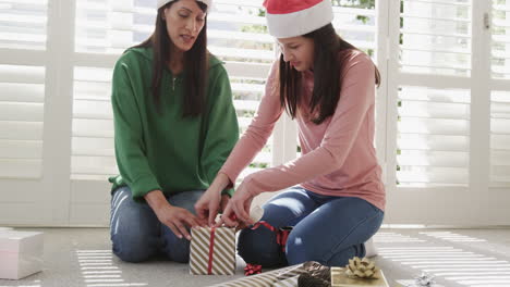 Happy-biracial-mother-and-adult-daughter-wrapping-christmas-gift-at-home,-copy-space,-slow-motion