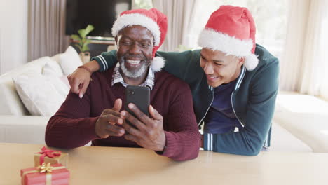 Glücklicher-Afroamerikanischer-Vater-Und-Sohn-In-Weihnachtsmützen-Mit-Smartphone-Videoanruf,-Zeitlupe