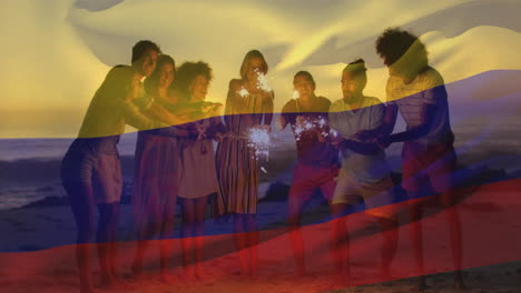 Animation-of-colombian-flag-waving-over-diverse-friends-with-sparklers-enjoying-at-beach