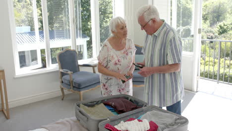 Senior-caucasian-couple-packing-suitcase-in-bedroom-at-home,-slow-motion