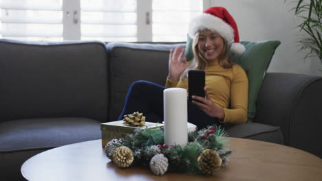 Feliz-Mujer-Birracial-Con-Sombrero-De-Santa-Usando-Un-Teléfono-Inteligente-En-Navidad,-Espacio-Para-Copiar,-Cámara-Lenta