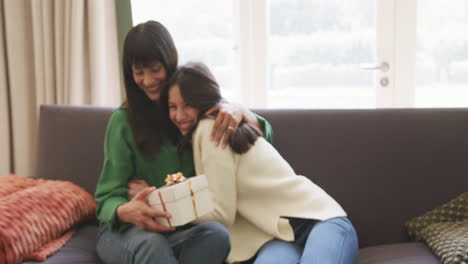 Happy-biracial-mother-and-adult-daughter-exchanging-christmas-gift-and-hugging,-slow-motion