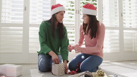 Happy-biracial-mother-and-adult-daughter-wrapping-christmas-gift-at-home,-copy-space,-slow-motion