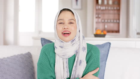 Happy-biracial-woman-in-hijab-waving-to-camera-at-home,-copy-space,-slow-motion