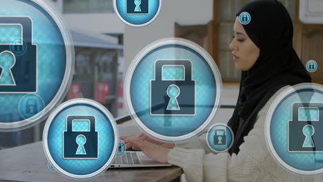 Animation-of-padlock-icons-over-biracial-woman-wearing-hijab-working-on-laptop-in-cafes