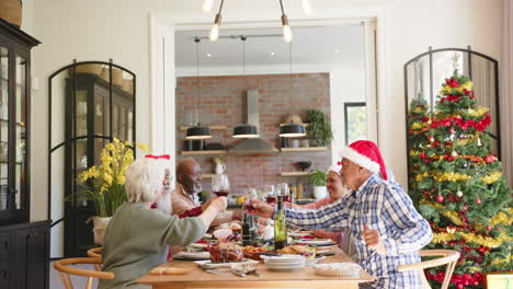 Happy-diverse-senior-friends-making-a-toast-with-wine-at-christmas-dinner,-copy-space,-slow-motion