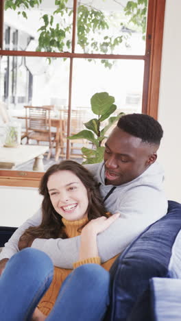Happy-diverse-couple-embracing-on-sofa-and-laughing,-slow-motion