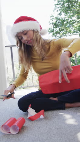 Vertical-video-of-biracial-woman-wearing-santa-hat-packing-christmas-presents,-slow-motion