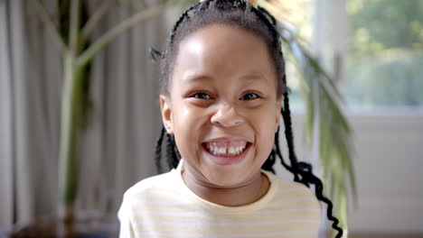Portrait-of-happy-african-american-girl-with-braided-hair-smiling-by-sunny-window,-slow-motion