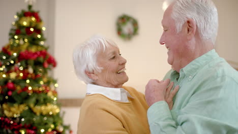 Happy-senior-caucasian-couple-dancing-next-to-christmas-tree-at-home,-slow-motion