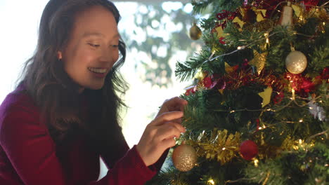 Glückliche-Biracial-Frau-Schmückt-Weihnachtsbaum-Und-Lächelt,-Zeitlupe