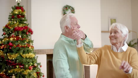 Happy-senior-caucasian-couple-dancing-next-to-christmas-tree-at-home,-slow-motion