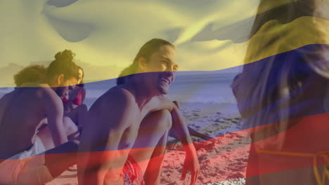 Animation-of-flag-of-colombia-waving-over-diverse-friends-sitting-and-enjoying-at-beach