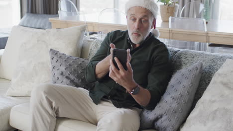 Kaukasischer-Mann-Mittleren-Alters-Mit-Weihnachtsmütze,-Der-Zu-Weihnachten-Zu-Hause-Sein-Smartphone-Benutzt,-Zeitlupe