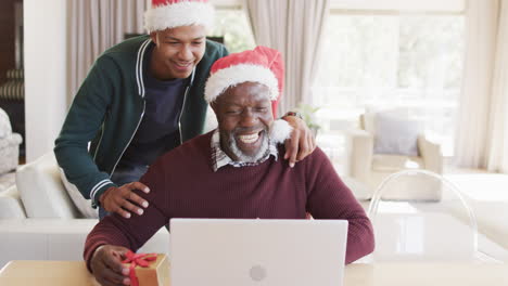 Glücklicher-Afroamerikanischer-Vater-Mit-Geschenk-Und-Sohn-Mit-Weihnachts-Laptop-Videoanruf,-Zeitlupe
