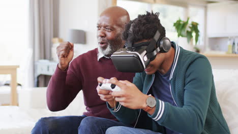 Glücklicher-Afroamerikanischer-Sohn-Mit-VR-Headset-Und-Gamepad-Mit-älterem-Vater-Zu-Hause,-Zeitlupe