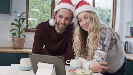 Vielfältiges-Paar-Mit-Weihnachtsmützen,-Das-Ein-Tablet-Für-Einen-Weihnachtsvideoanruf-In-Zeitlupe-Verwendet