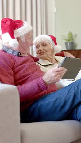 Video-Vertical-De-Una-Pareja-Caucásica-Mayor-Usando-Una-Tableta-Para-Videollamadas-Navideñas,-Cámara-Lenta