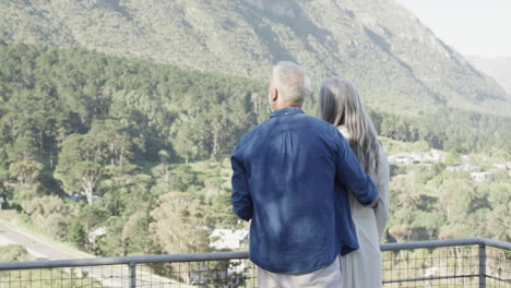 Glückliches-Kaukasisches-Paar-Mittleren-Alters,-Das-Auf-Einer-Terrasse-In-Den-Bergen-Redet-Und-Sich-Umarmt,-Zeitlupe