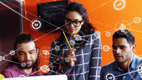 Animation-of-connected-globe-and-graph-icons-over-diverse-colleagues-looking-at-laptop-in-office