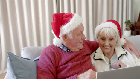 Senior-caucasian-couple-wearing-santa-hats-using-laptop-for-christmas-video-call,-slow-motion