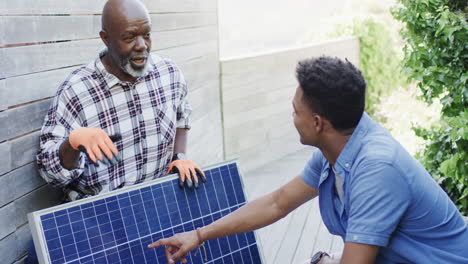 Padre-Afroamericano-Mostrando-Panel-Solar-A-Hijo-Adulto-En-Jardín-Soleado,-Cámara-Lenta