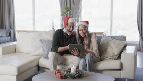 Kaukasisches-Paar-Mittleren-Alters-In-Weihnachtsmützen-Beim-Tablet-Videochat-Zu-Weihnachten-Zu-Hause,-Zeitlupe
