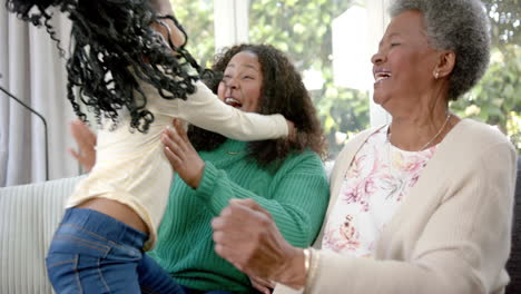 Happy-african-american-mother,-daughter-and-grandmother-on-couch-in-sunny-room,-slow-motion