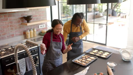 Happy-diverse-couple-in-aprons-baking-christmas-cookies-and-dancing-in-kitchen,-slow-motion