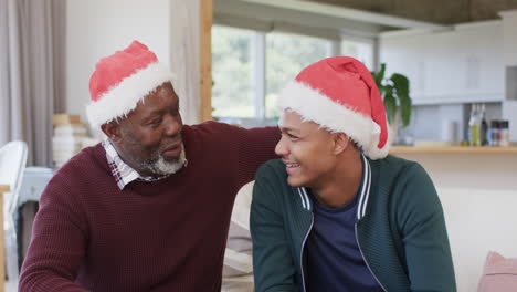 Happy-african-american-father-and-son-in-christmas-hats-having-video-call-and-embracing,-slow-motion