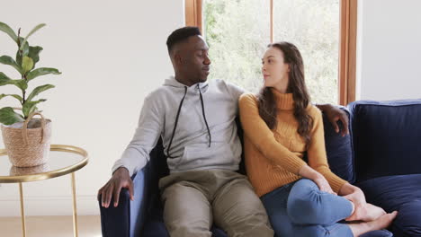 Happy-diverse-couple-sitting-on-sofa-talking-and-smiling-in-home,copy-space