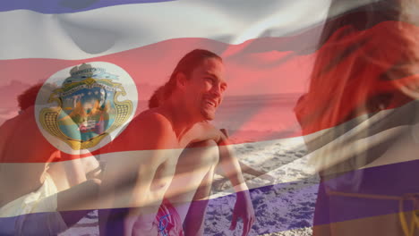 Animation-Der-Flagge-Costa-Ricas,-Die-über-Verschiedenen-Freunden-Weht,-Die-Am-Strand-Sitzen-Und-Spaß-Haben